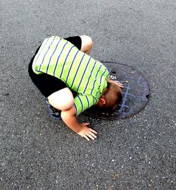 High angle view of boy touching head on manhole