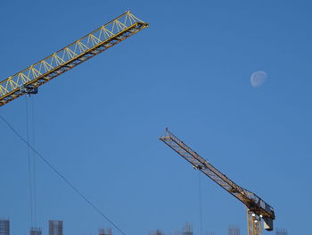 Low angle view of crane against clear blue sky