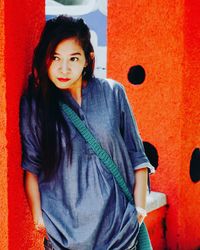 Portrait of smiling young woman standing against red wall