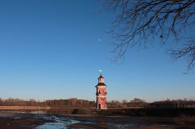 Lighthouse by building against clear blue sky