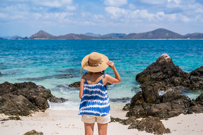 Rear view of woman wearing hat standing at beach against sky