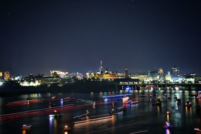 Illuminated buildings by river against sky at night