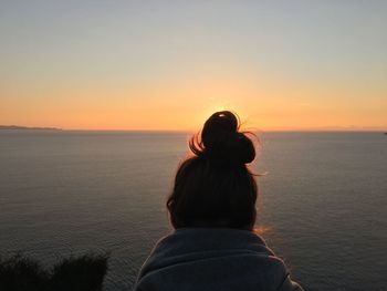 Rear view of woman against sea during sunset