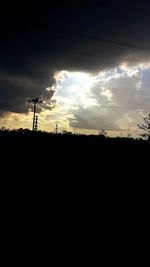 Silhouette electricity pylons on field against sky during sunset