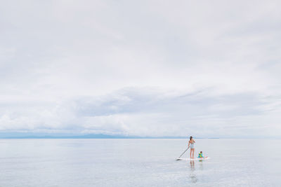 Mother with son paddleboarding in sea against sky