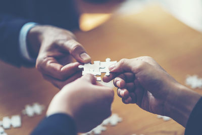 Cropped hands of business colleagues playing jigsaw puzzle at desk in office