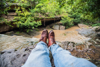Low section of man relaxing against stream at forest