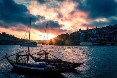 Sailboats moored on harbor in city against sky during sunset