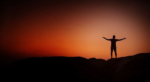 Silhouette man with arms outstretched standing against sky during sunset