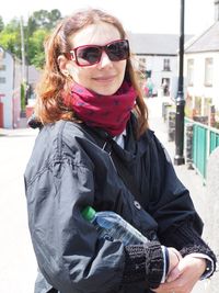 Smiling young woman wearing jacket and scarf standing on road against buildings during sunny day