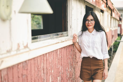 Portrait of smiling young woman standing against wall