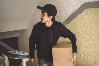 Delivery man with package looking away while walking on staircase