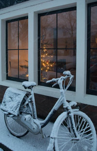 Bicycle by window of building during winter at night