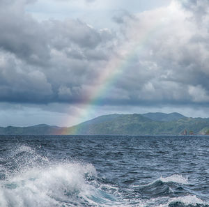 Scenic view of rainbow over sea against cloudy sky