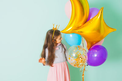 Full length of girl standing with balloons against wall