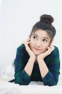 Smiling young woman looking away while lying on bed at home