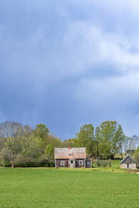 House on field by trees against sky