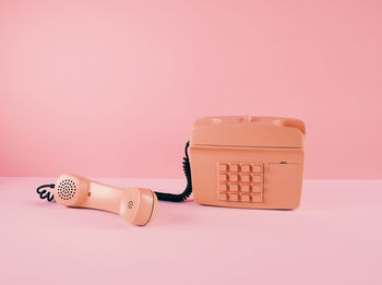 Close-up of telephone booth on table against pink background