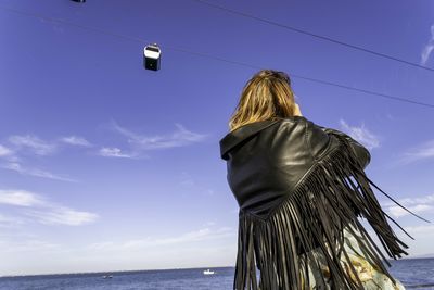 Rear view of woman standing by sea against sky