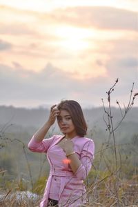 Portrait of young woman standing against sky during sunset