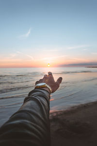 Midsection of man on beach against sky during sunset