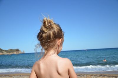 Rear view of shirtless girl against sea at beach