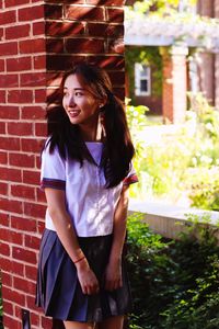 Portrait of smiling young woman standing against brick wall