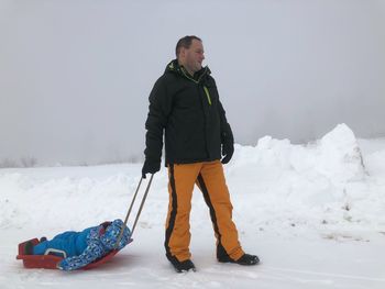 Father pulling sled with son on snowy field