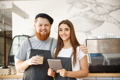 Portrait of smiling young woman using mobile phone while standing in cafe