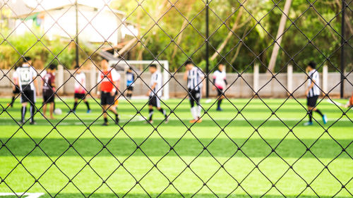 Men playing soccer on field seen through chainlink fence