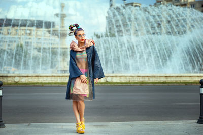 Full length of woman standing against dancing fountain on road