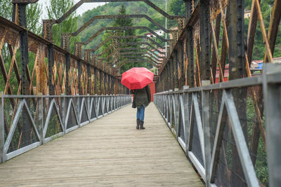 Rear view of woman with umbrella walking on covered bridge