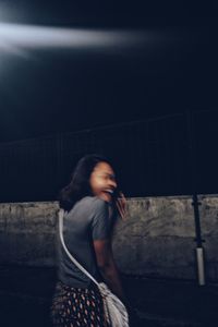 Side view of woman standing against wall at night