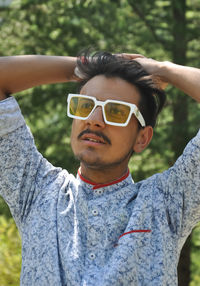 A handsome young guy wearing sunglasses posing outdoors with hands on hair with looking sideways