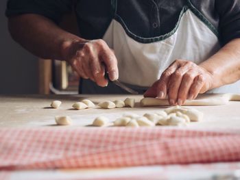 Cropped hands of woman cutting dough in kitchen