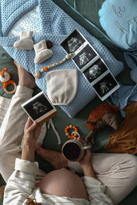 Top view of pregnant woman is preparing baby clothes for a newborn and considering ultrasound images