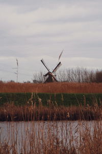 Wind turbines on field by lake against sky