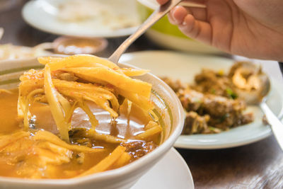 Close-up of hand holding soup in bowl on table