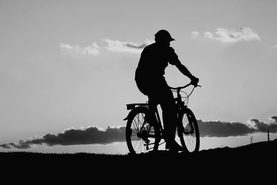 Silhouette man riding bicycle on field against sky