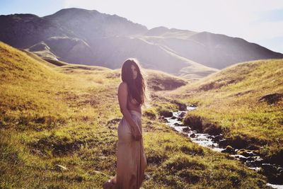 Side view of woman standing on grass against mountains and sky