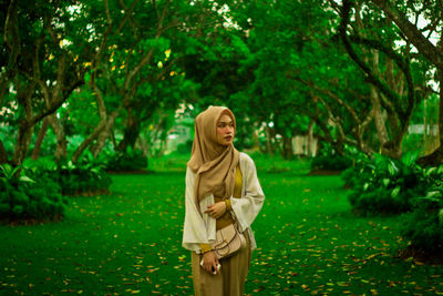 Young woman standing by plants against trees