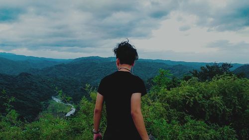 Rear view of young man standing on mountain against cloudy sky