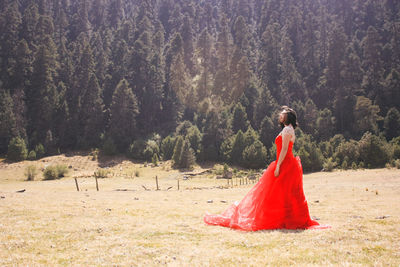 Woman in red gown standing on field at forest