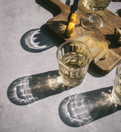 Top view composition with glasses of wine served with sliced cheese and bread with jam on marble table with wooden board in sunlight