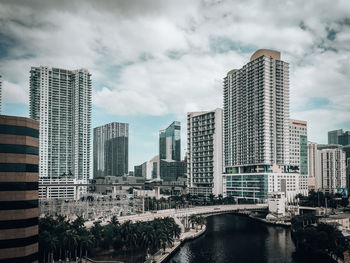 Modern buildings by river against sky in city