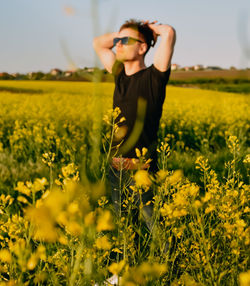 Rear view of woman standing amidst yellow flowering plants on field