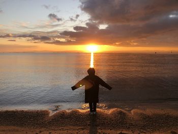 Rear view of man standing at beach during sunset