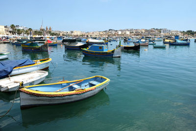 Boats moored at harbor against clear blue sky