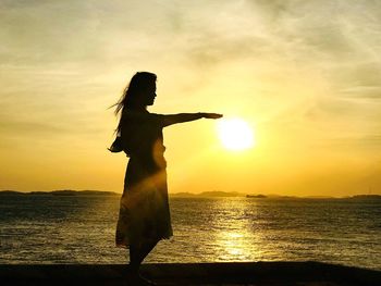 Silhouette woman standing at sea against sky during sunset