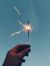 Hand holding sparkler against sky